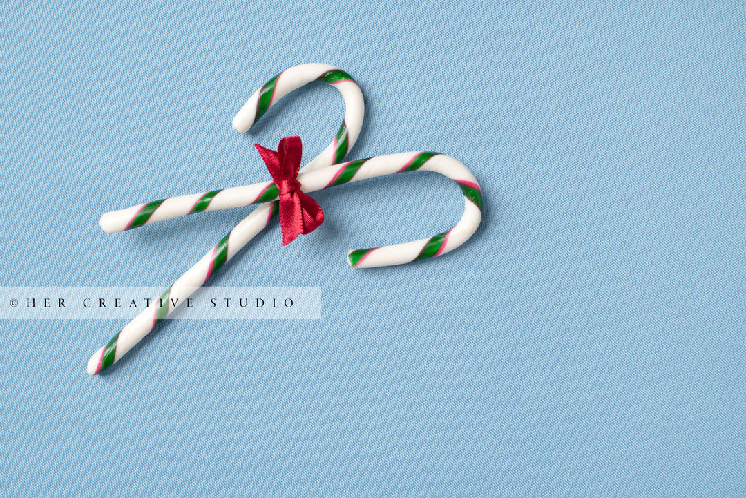 Two Candy Canes & Red Bow on Sky Blue Background