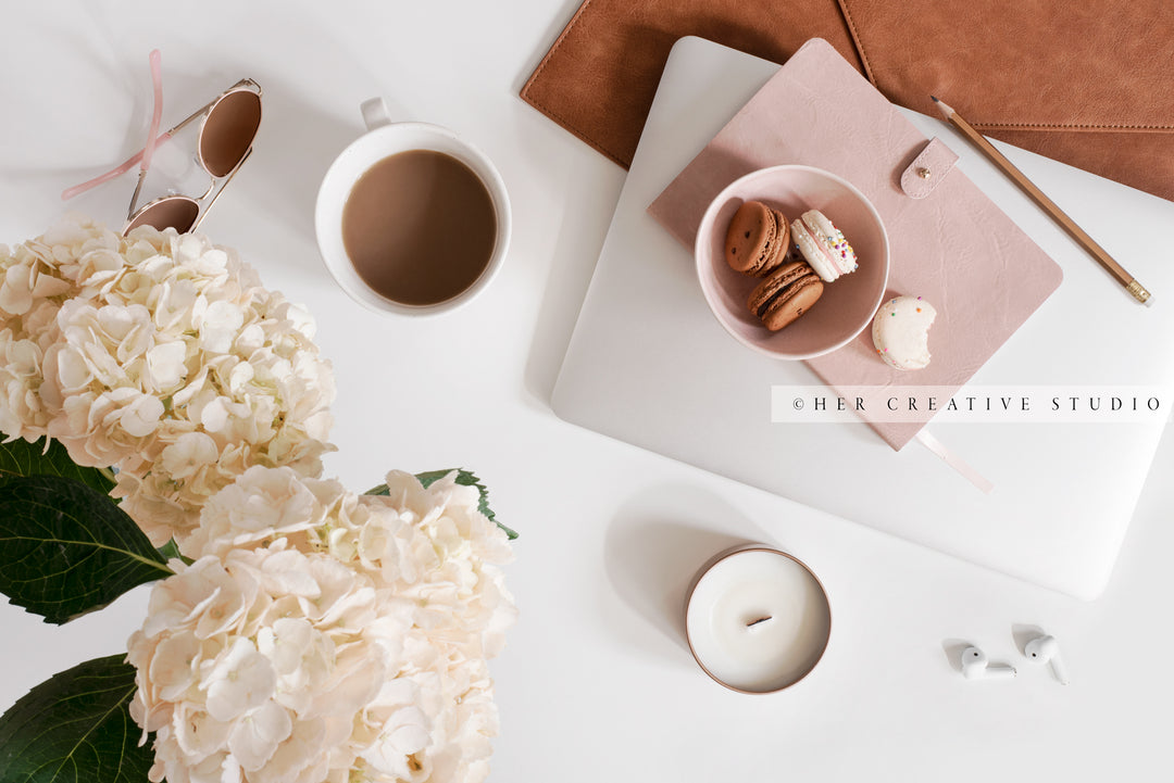 Candle, Hydrangea & Macarons on White Workspace. Digital Image.